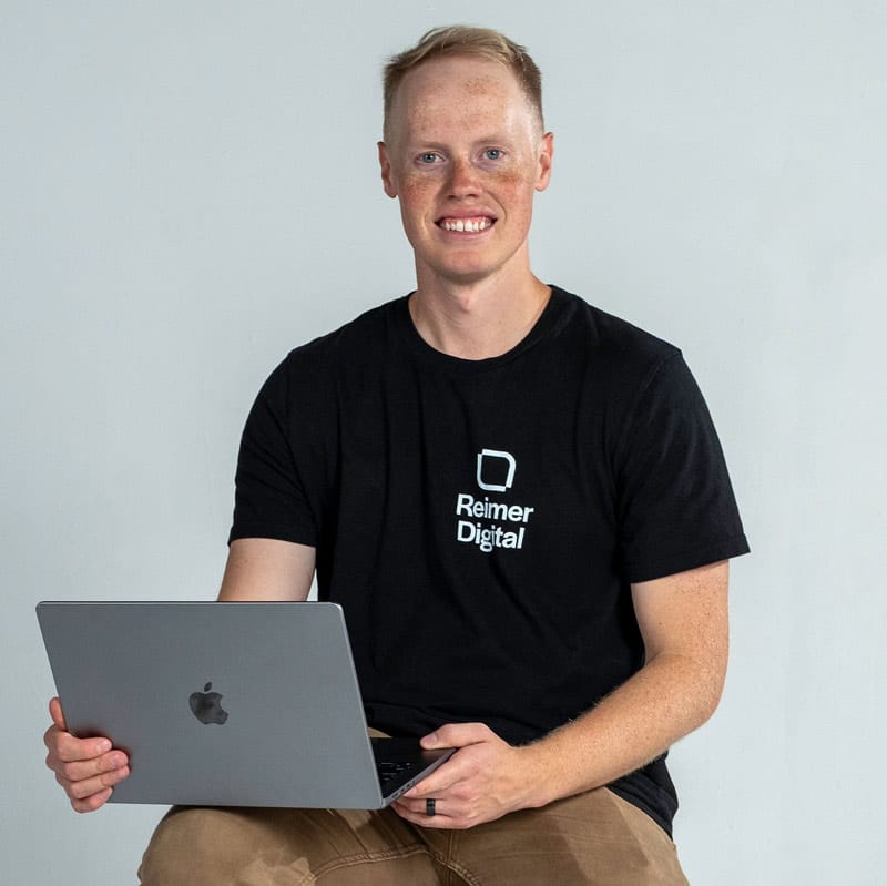 Matthew Reimer sitting with laptop looking into camera.